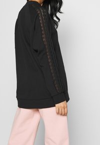 Svart sweatshirt med spetsdetaljer på ärmarna, med en avslappnad passform och ribbade mudd. Tillsammans med ljusrosa byxor.