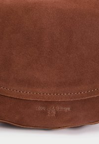 Brown suede leather bag section showing curved edge with visible stitching and embossed brand name with logo.