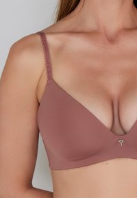 Reggiseno color rosa con coppe lisce e imbottite, e un charm dorato decorativo al centro. Le spalline regolabili presentano il logo del marchio.