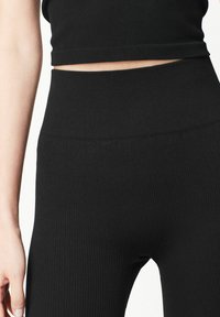 Leggings noirs à côtes avec une taille haute et une texture lisse. Le design est ajusté sans qu'il y ait de matériel ou d'accents visibles.