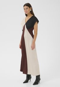Maxi haljina s V-izrezom u crnoj, krem i burgundijskoj boji s blokovima boja. Ima kratke rukave u obliku kapa i lepršavu satensku teksturu. Crne čizme na petu.