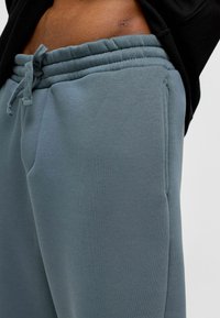 Lichtblauwe-grijze joggingsbroek gemaakt van zachte stof, met een elastische tailleband en verstelbare trekkoord, en zijkiezen.