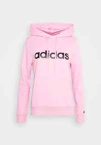 Jasnoróżowa bluza z kapturem z czarnym logo "adidas" z przodu, wyposażona w kieszeń kangurkę i ściągacze przy rękawach. Miękki materiał i casualowy design.