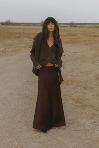 Burgundi spalvos maksi sijonas su tekstūruotu audiniu, derinamas su tamsiai rudos spalvos kardiganu su mygtukais. Natūralus peizažas su sausa žole ir žvyru.