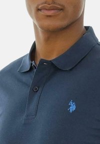 Navy polo shirt made of cotton with a smooth texture; features a three-button placket and a blue embroidered logo on the left chest.
