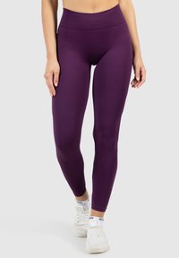 Leggings viola a vita alta realizzati in materiale elastico, con una texture liscia e un design aderente, abbinati a scarpe da ginnastica bianche.