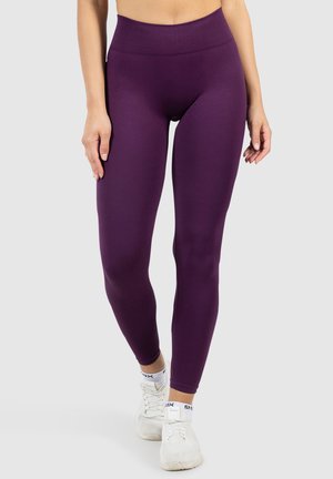 Leggings viola a vita alta realizzati in materiale elastico, con una texture liscia e un design aderente, abbinati a scarpe da ginnastica bianche.