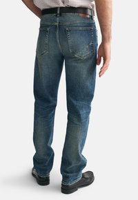Blå denimjeans med rak passform, slitna detaljer på bakfickorna och en brun läderlapp vid midjan.