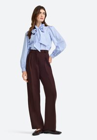 Blauw-witte geblokte blouse met een grote strik, gecombineerd met hoog getailleerde bruine wijdvallende broek en zwarte instapschoenen.
