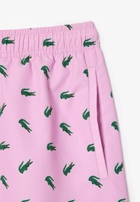 Pantaloni corti rosa con un motivo ripetuto di coccodrilli verdi, cintura elastica e tasca laterale, realizzati in un tessuto leggero e liscio.
