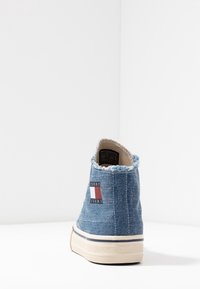 Džínová vysoká obuv s třepeným límcem, s červeným, bílým a modrým logem. Světle modrá barva s béžovou gumovou podrážkou a švy.