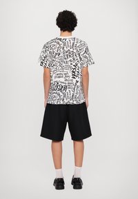 Melna un baltā kratovā t-krekls ar grafisku tekstu. Saskaņots ar līdz ceļiem melniem šortiem un melnām kurpēm.