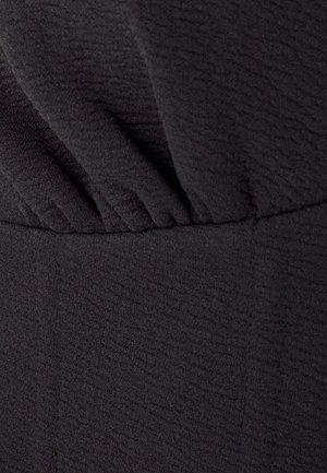 Tissu noir texturé avec des détails plissés au niveau du col et une taille lisse. Le matériau semble doux et légèrement extensible.