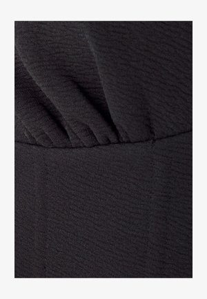 Tissu noir texturé avec des détails plissés au niveau du col et une taille lisse. Le matériau semble doux et légèrement extensible.