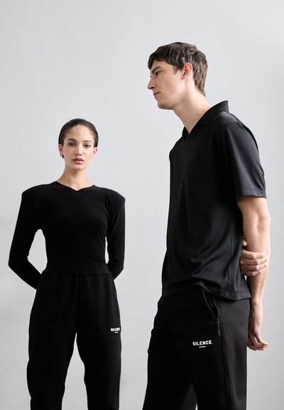 Svart långärmad topp och svart kortärmad polo skjorta bärs med matchande svarta joggers. Innehåller elastisk midja och tryckt textdetalj.