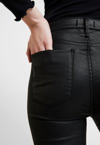 Černé džíny z denimu s přiléhavým střihem, pěticípým stylem a hladkou texturou. Zadní kapsa je obšita kontrastním stehem.