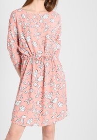 Blommig klänning i korall med vitt och svart blommönster, med lös passform, tre fjärdedelsärmar och elastisk midja.