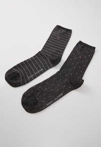 Schwarze Socken mit einer strukturierten Oberfläche; eine Seite hat dünne horizontale Streifen, die andere Seite weist ein Punktmuster auf. Markenname sichtbar.