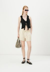 Svart kort topp med volanger, beigefargede elastiske shorts, svarte snørelaterte flate sko og en veske med slangeskinnsmønster. Modellen har på seg solbriller.