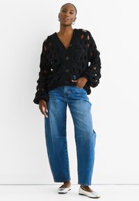 Black knitted cardigan with open pattern, long sleeves, and buttons. Paired with loose blue jeans and silver ballet flats.