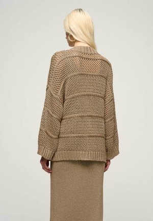 Beige open-knit trui met een losse pasvorm, geribbelde manchetten en een gestructureerd ontwerp. Gecombineerd met een bijpassende metallic rok.