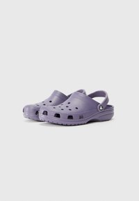 Purple clogs with a closed toe, back strap, and ventilation holes. Made from lightweight material with a textured surface and flat sole.
