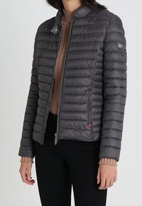 Szara kurtka puchowa z zamkiem błyskawicznym, prążkowanym kołnierzem, poziomymi szwami i kieszeniami bocznymi. Materiał wydaje się lekki i elegancki.