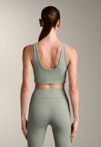 Top corto a coste e leggings a vita alta in verde salvia. Presenta un design con scollo a barca e una texture elegante con una fascia elastica in vita.