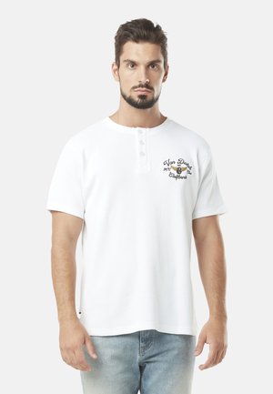 T-shirt henley blanc avec un col rond, des manches courtes, un patte de boutonnage à trois boutons et un design de texte brodé sur la poitrine gauche.