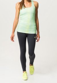 Jasnozielony top na ramiączkach w poziome paski, w połączeniu z czarnymi legginsami. Obuwie to żółte buty sportowe.