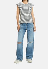 Pruhovaný top s krátkými rukávy v bílé a černé, s volnými světle modrými roztrhanými džínami, doplněný robustními bílými teniskami.