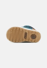 Semelle en caoutchouc avec un grip texturé, de couleur beige clair. La tige comprend des matériaux bleus et marine foncé avec des accents orange et des détails de couture.
