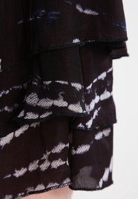 Tissu noir en couches avec des motifs abstraits blancs et bleus. Texture douce et légère avec des bords froncés et des détails de couture contrastants.
