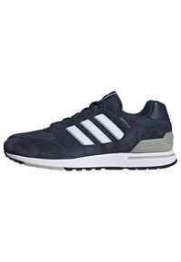 Tumši zili zamšādas sneakers ar baltām acs paneļiem, trim baltām svītrām, mīkstu potīti un kontrastējošu pelēku papēža daļu.