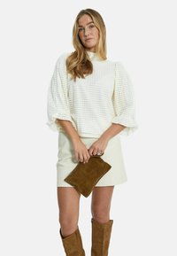 Vit texturerad tröja med puffärmar, matchad med en beige minikjol och en brun mocka clutch. Modellen bär bruna knähöga stövlar.