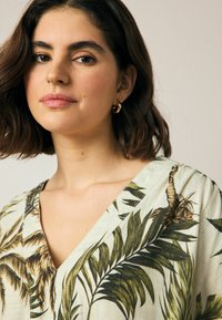 Bluse mit floralem Muster aus leichtem Stoff, die grüne Palmblätter zeigt, einen tiefen V-Ausschnitt und kurze Ärmel hat, mit einer lässigen Passform.