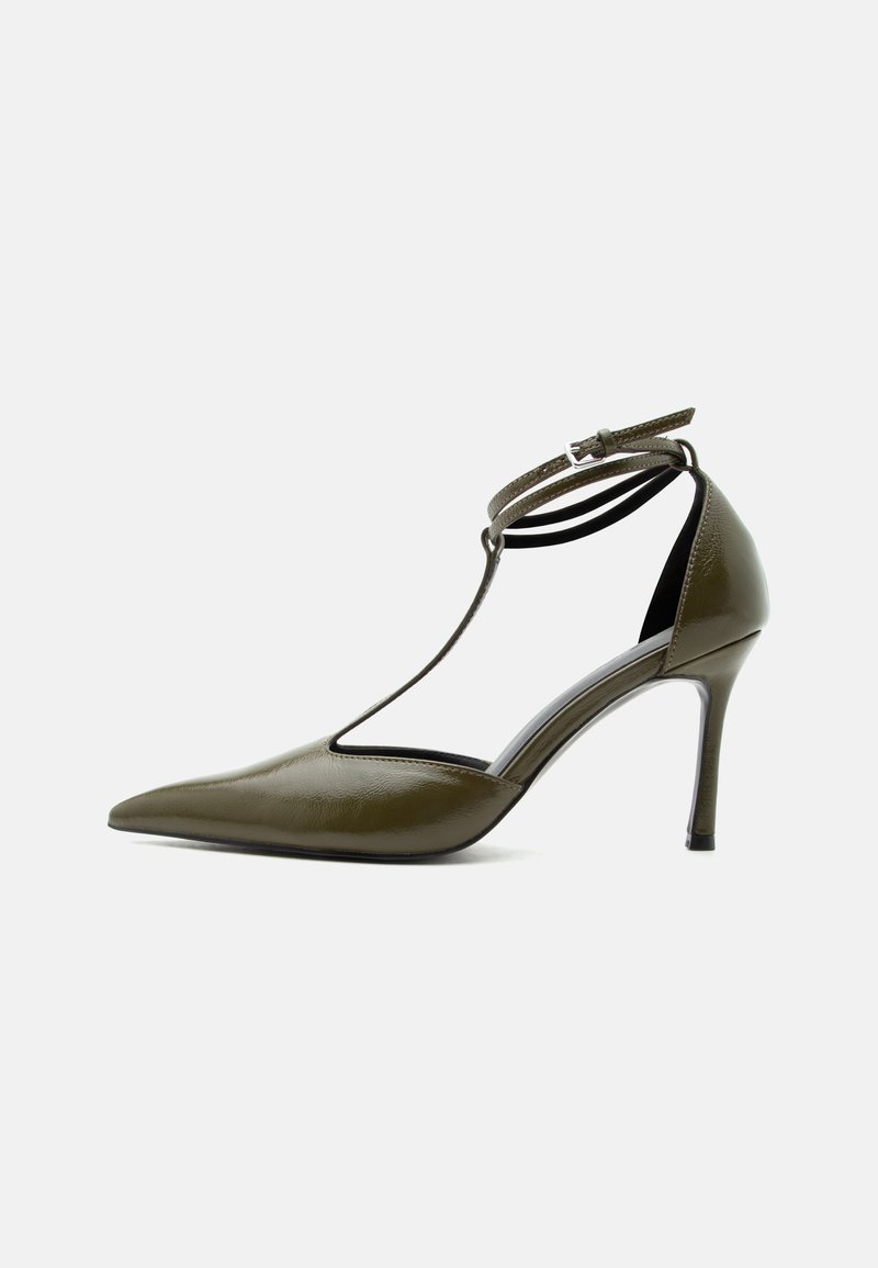 Chaussure à talon haut vert olive à bout pointu avec bride à la cheville et design à bride en T, finition brillante, talon stiletto fin, sur fond blanc.