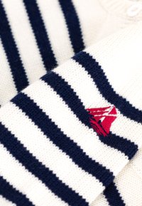 Gebreid sweater met marineblauwe en witte horizontale strepen, voorzien van een klein rood logo detail. Zachte textuur en ontwerp met een geknoopte kraag.