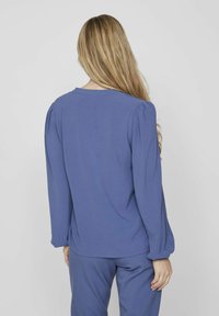 Dolga majica iz enotne modre tkanine z okroglim izrezom in nabranim detajlom na ramenskih šivih. Mehek material, sproščen kroj.