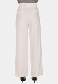 Pantaloni bianchi a gamba larga con tessuto liscio e strutturato, caratterizzati da vita alta e passanti per cintura, mostrati da dietro con due tasche posteriori.