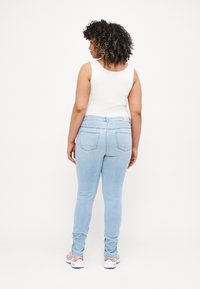 Jeans skinny de color azul claro con una textura suave, que cuentan con bolsillos traseros y una cintura de altura media, combinados con una camiseta sin mangas blanca.
