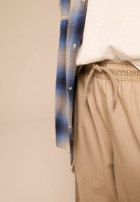 Camicia a quadri blu e bianca indossata su una t-shirt bianca, abbinata a pantaloni corti beige con vita elasticizzata e dettaglio con coulisse.