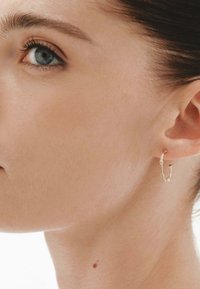 Pendientes de aro de oro con diseño retorcido, que presentan una superficie texturizada y acentos sutiles, exhibidos en la oreja de un modelo.