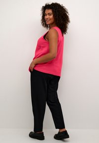 Pink sleeveless top with a loose fit, paired with black tapered pants and black shoes. Background is a neutral color.