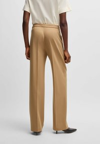 Wide-leg trousers in a light brown shade, made from smooth fabric. Features a high waist and paired with sleek black heels.