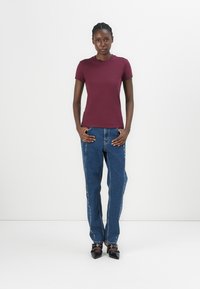 Tricou scurt de culoare vișinie cu guler rotund, asociat cu blugi decolorati cu talie inalta, cu cusături laterale și pantofi cu toc negri.