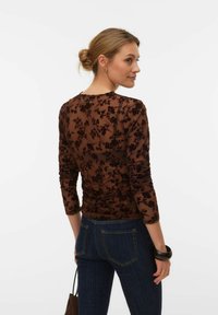 Haut en maille marron avec broderie florale, manches longues et texture plissée, associé à un jean bleu foncé. Vue de dos montrant la coupe et le style.