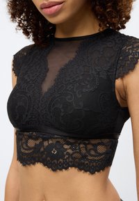 Μαύρο σουτιέν από δαντέλα με διαφανές δίχτυ στο πάνω μέρος και κοντά μανίκια, διακοσμημένο με λουλουδένια σχέδια και τελείωμα από οδοντωτή δαντέλα. Μαλακό ύφασμα.