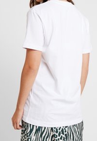 Vit kortärmad t-shirt i bomull, med en klassisk rund halsringning, som har en slät yta och inga synliga grafiska element eller detaljer.