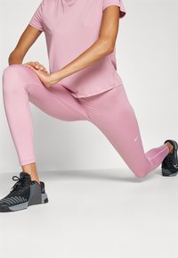 Top sportivo rosa e leggings realizzati in tessuto elasticizzato, con cuciture piatte. Scarpe da ginnastica nere con design testurizzato e lacci.